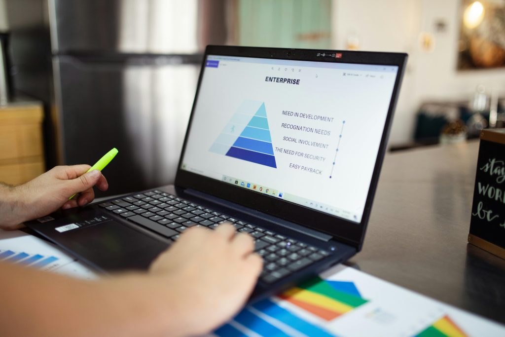 Person analyzes business data on laptop, using pyramid chart and financial reports.