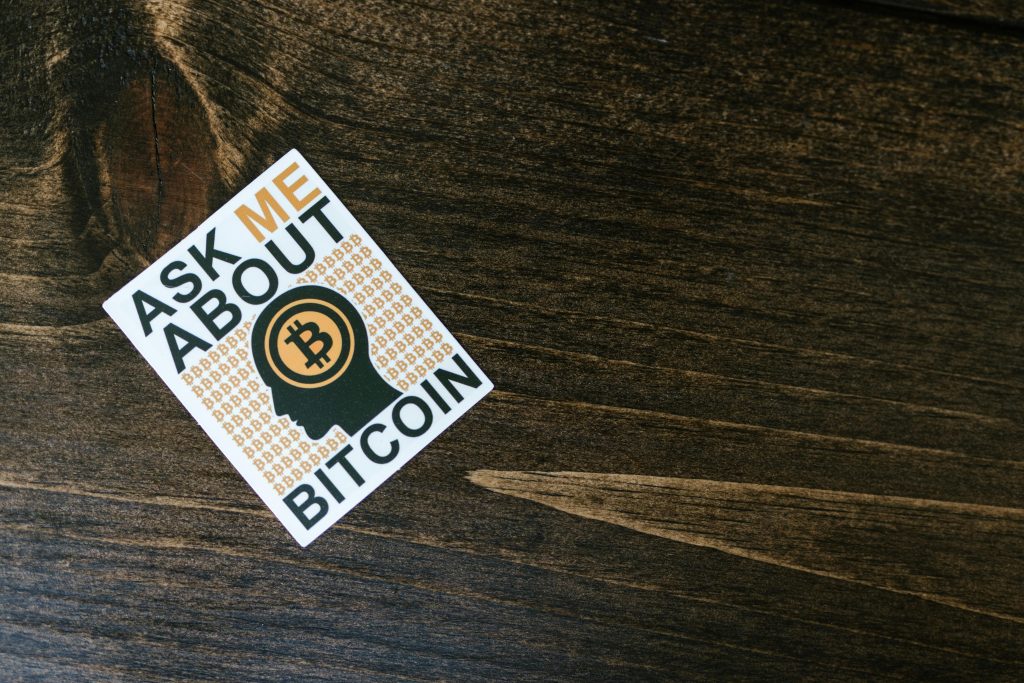 A sticker with Bitcoin theme on a wooden table surface, promoting cryptocurrency discussion.